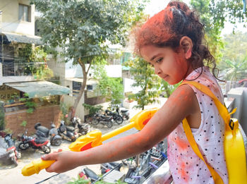 Sweet little indian girl playing colours on holi festival, holding pichakaree full of colours