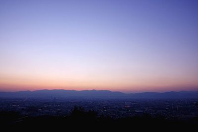 Cityscape and silhouette mountain range against sky during sunset