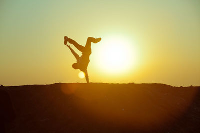 Silhouette person doing handstand against sky during sunset