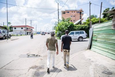 Rear view of friends walking on street against cloudy sky