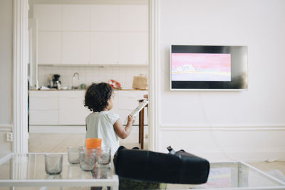 Rear view of girl with remote control watching tv at home