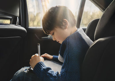 Side view of boy studying while sitting in car