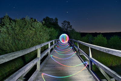 Lightpainting on a footbridge over trees against sky