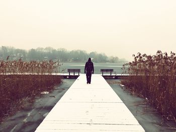 Rear view of man walking on pier over frozen lake against clear sky