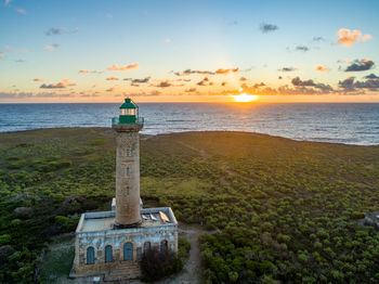 Lighthouse by sea against sky during sunset
