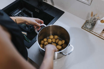 Woman's hands washing potatoes in saucepan