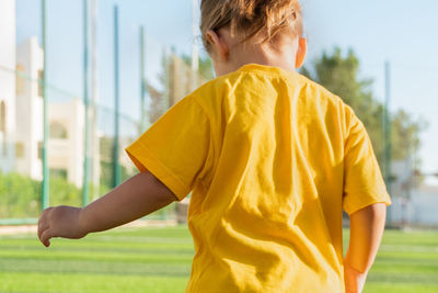 Faceless little girl in yellow t-shirt playing football.