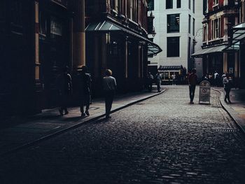 Rear view of people walking on street amidst buildings in city