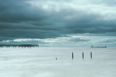 Wooden posts in sea against sky