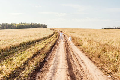 Dirt road passing through agricultural field against sky