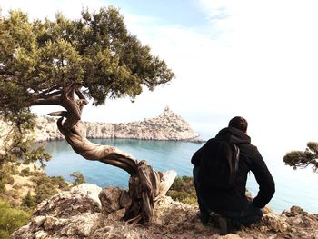 Man sitting on rock by sea against sky