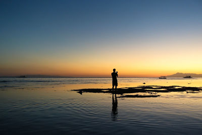 Silhouette man standing at beach against clear sky during sunset