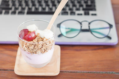 Close-up of granola with plum and coconut in glass against laptop