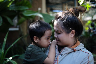 Mother carrying son while standing by plants