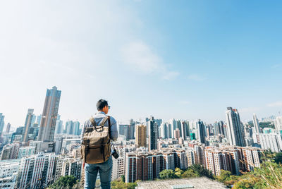 Rear view of man standing by cityscape against sky