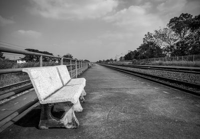 Empty benches by railroad tracks against sky