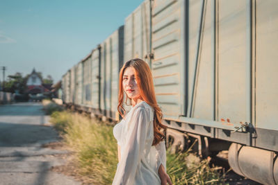 Portrait of woman standing by car against sky