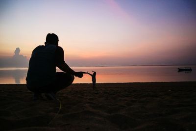 Optical illusion of giant man touching tiny woman gesturing while standing on shore at beach during sunset