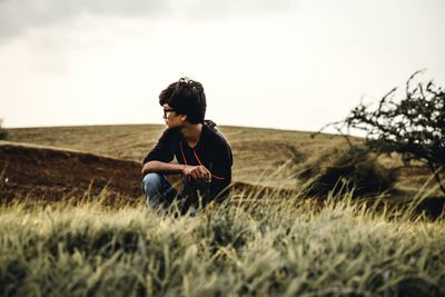 Boy looking away while sitting on land