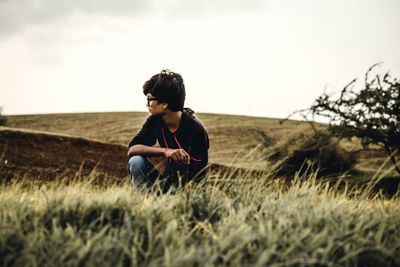 Young man looking away while sitting on field