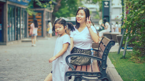 Portrait of smiling woman showing peace sign by daughter at beach