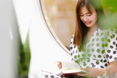 Smiling young woman reading book while sitting outdoors