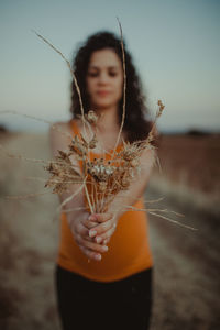 Close-up of young woman holding plants against sky