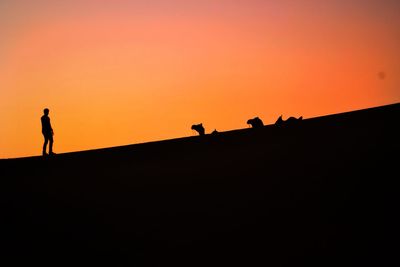 Silhouette people standing on land against orange sky