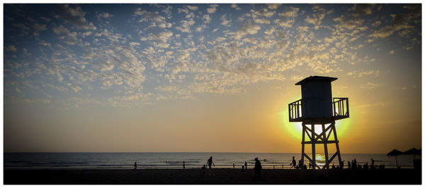 Silhouette lifeguard hut on beach against sky during sunset