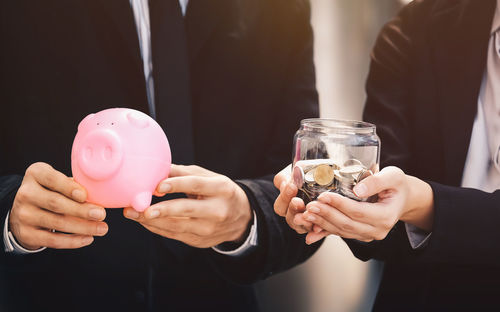 Midsection of business people holding piggy bank and coins in jar