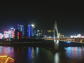 Illuminated bridge over river by buildings against sky at night