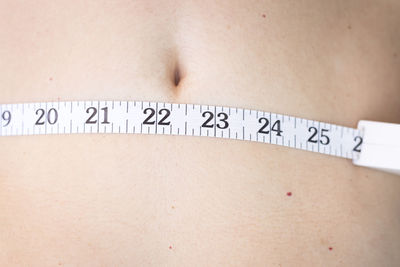 Midsection of shirtless woman measuring waist at home