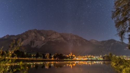 Illuminated buildings by mountains against sky at night