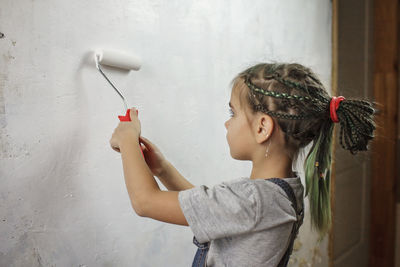 Side view of girl holding umbrella standing against wall at home