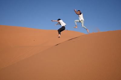 Low angle view of friends jumping in desert against clear sky