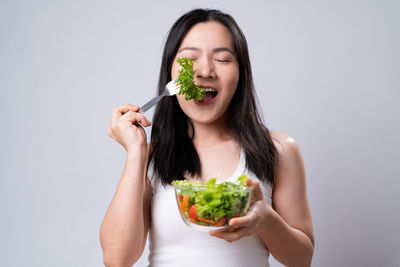 Portrait of woman eating food against white background