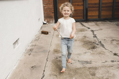 Full length portrait of happy girl playing with magic wand outside house