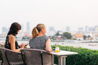 Rear view of women sitting in city against sky