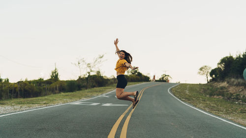 Full length of woman jumping on road against clear sky