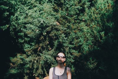 Portrait of young woman standing against plants