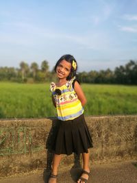 Portrait of smiling girl standing on road against field