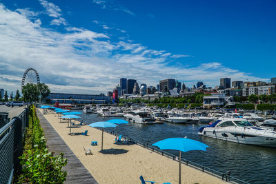 Boats moored in river by buildings against blue sky