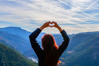 Rear view of woman with arms raised against mountains