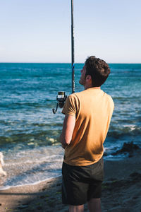 Rear view of man standing at beach against sky