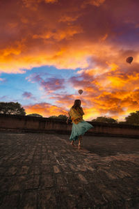 Rear view of woman standing on land against sky during sunset