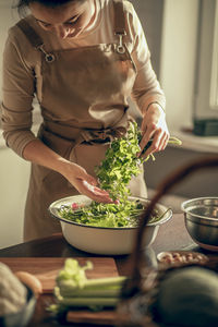 A young woman in an apron in the kitchen is washing parsley greens for a vegan morning