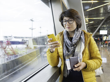 Woman with passport and boarding pass is texting on her smartphone. tourist waits for boarding.