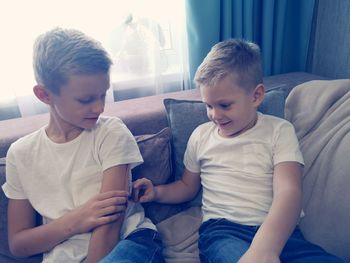 Brothers playing at home while sitting on sofa