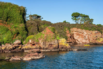 Scenic view of rocks by sea against clear sky