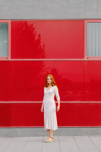 Full length portrait of woman standing against red wall